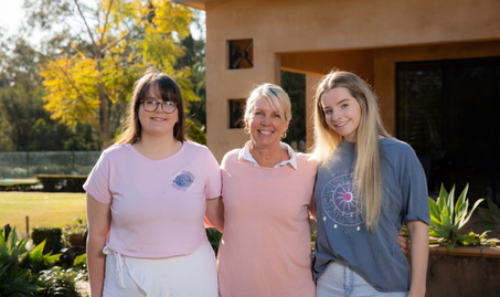Heidi Morris and two of her daughters standing in their front yard smiling into the camera.
