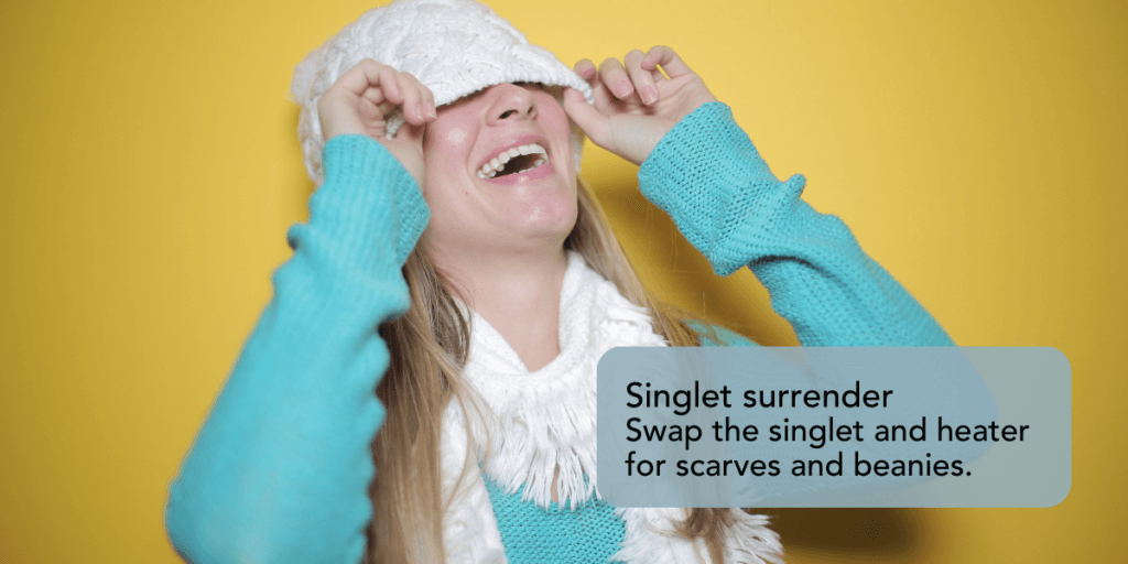 A woman wearing a jumper and beanie. On-image text reads: 'Singlet surrender. Swap the singlet and heater for scarves and beanies.'